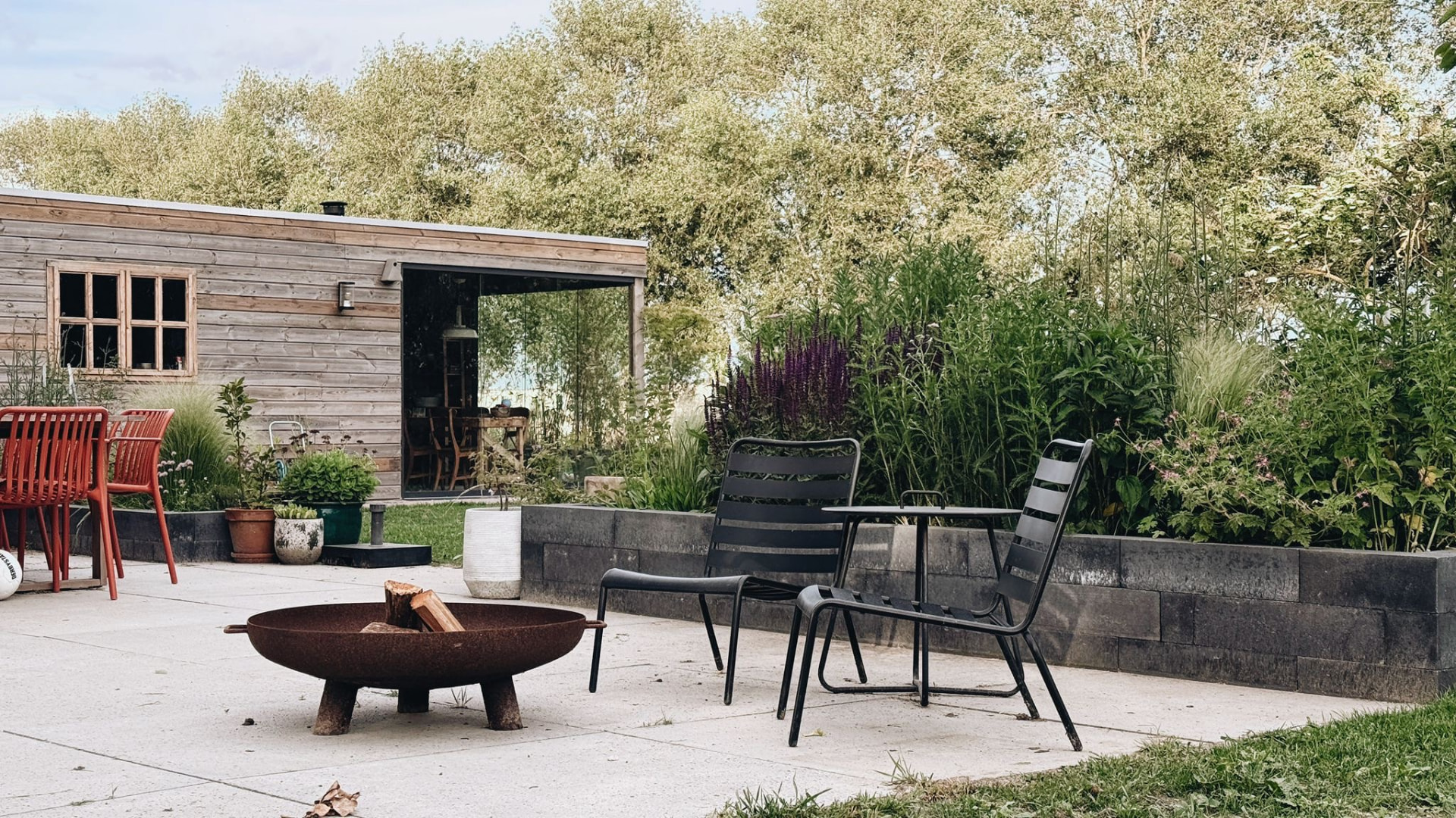 Terras met vuurschaal en stoelen langs een border met salie en siergrassen