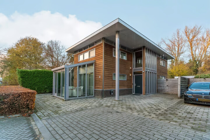 Vooraanzicht van de woning met oprit en bestaande beukhaag